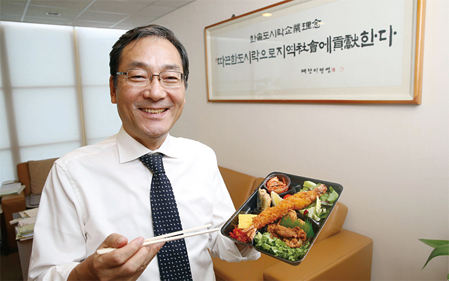 이영덕 한솥 회장이 도시락을 소개하며 활짝 웃고 있다. 이 회장 뒤로 ‘따끈한 도시락으로 지역사회에 공헌한다’는 한솥의 기업이념이 적혀있다. 사진 조선일보 DB