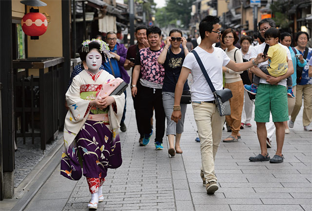 가장 일본적인 거리로 유명한 교토의 기온 거리를 걸어가는 게이코(교토에서 게이샤를 일컫는 명칭)를 관광객들이 지켜보고 있다.