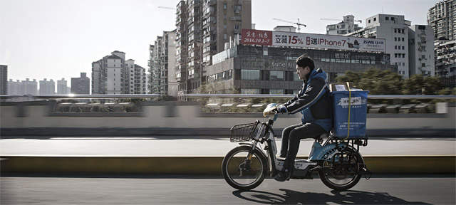 지난 2월 중국 상하이에서 ZTO익스프레스 직원이 택배 상자를 실은 전기자전거에 올라 도로를 달리고 있다. <사진 : 블룸버그>