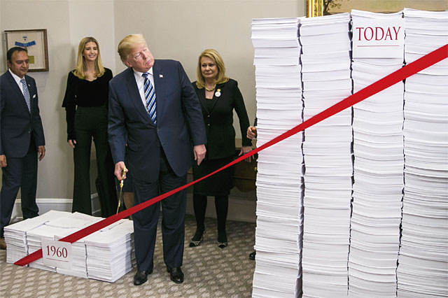 트럼프가 지난해 12월 미국 백악관 루스벨트룸에서 규제를 상징하는 하얀 서류 뭉치 위에 둘러져 있는 빨간 테이프를 가위로 자르는 이색 퍼포먼스를 하고 있다. <사진 : 블룸버그>