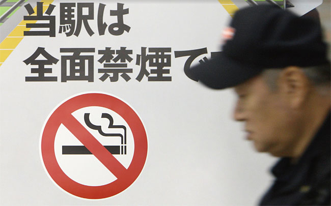 일본 도쿄의 한 거리에 붙어있는 ‘금연’ 표식 옆으로 한 노인이 지나가고 있다. 사진 블룸버그