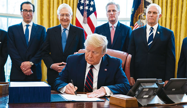 도널드 트럼프 미국 대통령이 3월 27일(현지시각) 백악관 집무실에서 코로나19 대응을 위한 2조2000억달러(약 2700조원) 규모의 경기 부양 패키지 법안에 서명하고 있다. 사진 AP연합