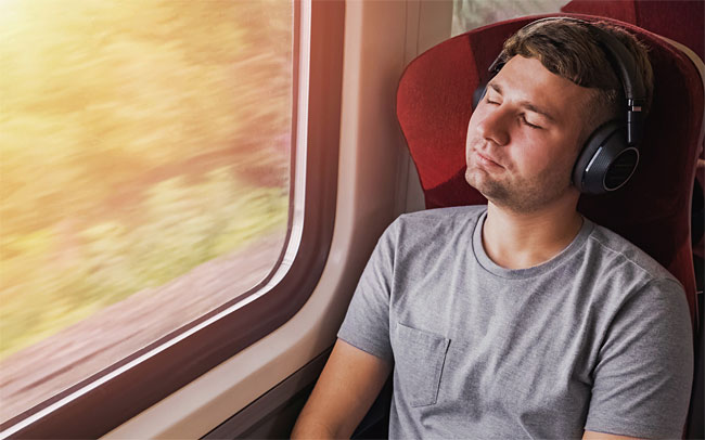 노이즈 캔슬링 기능이 탑재된 헤드폰을 쓴 남성이 기차에서 휴식을 취하고 있다.