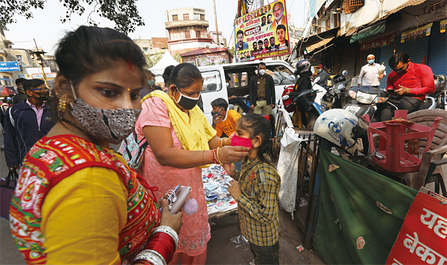 코로나19 확산세가 진정되면서 인도 경제가 예상보다 빠르게 회복하고 있다. 인도 뉴델리의 시장에서 한 여성이 딸에게 마스크를 씌워주고 있다. 사진 AP연합