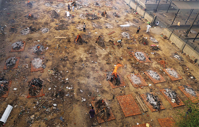 4월 21일(현지시각) 인도 뉴델리의 한 화장터에서 장례용 화약을 태우는 가운데 코로나19로 사망한 주검이 누워 있다. 왼쪽 아래는 나렌드라 모디 인도 총리. 사진 블룸버그·EPA연합