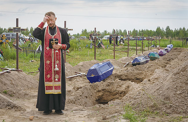 우크라이나의 수도 키이우 외곽에 있는 부차에서한 사제가 러시아군에게 살해당한 신원 미상의 민간인 희생자들을 위해 기도하고 있다. 사진 AP연합