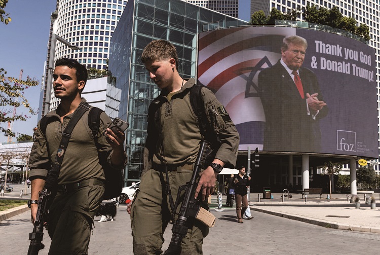 이스라엘 군인들이 2026년 3월 12일 이스라엘 텔아비브에서 'Thank you God & Donald Trump'라는 문구가 적힌 광고판 옆을 지나가고 있다. /사진 로이터연합